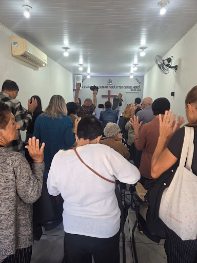 Pessoas congregando em oração com mãos erguidas no templo da Taquara